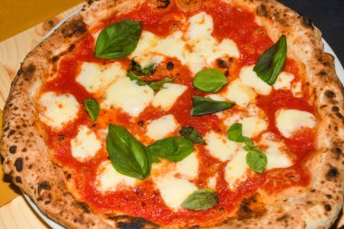 Pizza Margherita, San Marzano domatesleri, mozzarella peyniri, taze fesleğen, tuz ve ekstra bakire zeytinyağından yapılmış tipik bir Napoli pizzasıdır. Dilimlenmemiş bir parça, restoranda bir tabakta servis edilmiş.