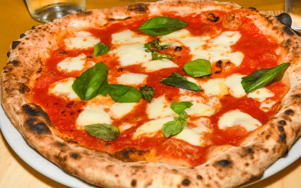 Pizza Margherita is a typical Neapolitan pizza, made with San Marzano tomatoes, mozzarella cheese, fresh basil, salt and extra-virgin olive oil. Whole unsliced piece, served on a plate in restaurant