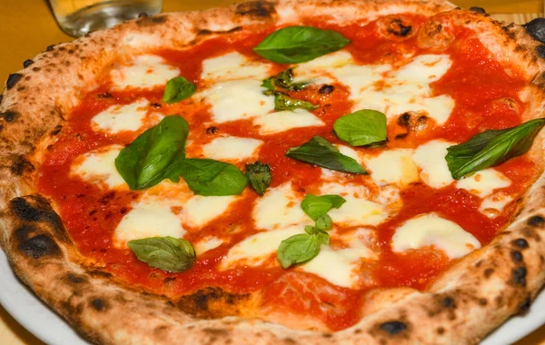 Pizza Margherita is a typical Neapolitan pizza, made with San Marzano tomatoes, mozzarella cheese, fresh basil, salt and extra-virgin olive oil. Whole unsliced piece, served on a plate in restaurant