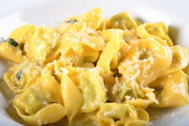 Peynirli ve ıspanaklı Tortellini, tereyağı, adaçayı sosu, rendelenmiş parmesan. Geleneksel İtalyan makarnası üzerine Parmigiano-Reggiano gevrekleri, beyaz tabakta, restoranda kahverengi masada servis ediliyor.