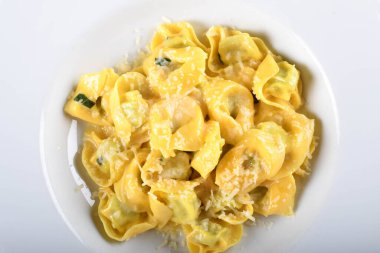 Peynirli ve ıspanaklı Tortellini, tereyağı, adaçayı sosu, rendelenmiş parmesan. Geleneksel İtalyan makarnası üzerine Parmigiano-Reggiano gevrekleri, beyaz tabakta, restoranda kahverengi masada servis ediliyor.