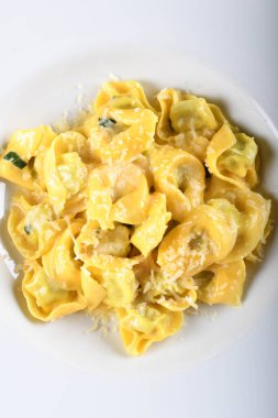 Peynirli ve ıspanaklı Tortellini, tereyağı, adaçayı sosu, rendelenmiş parmesan. Geleneksel İtalyan makarnası üzerine Parmigiano-Reggiano gevrekleri, beyaz tabakta, restoranda kahverengi masada servis ediliyor.