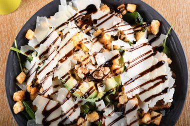 Bebek ıspanak salatası, avokado, kiraz domatesleri, mantarlar, salatalık sosu, kıtır ekmek, parmezan, kavrulmuş ceviz, kahverengi ahşap bir masada servis edilen siyah bir kase, İtalyan restoranı.