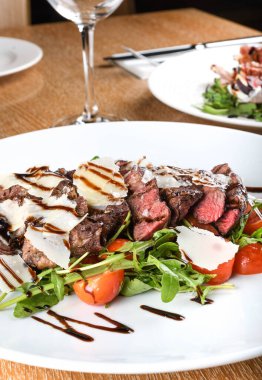 Geleneksel İtalyan ana yemeği. Tagliata bifteği, roka, kiraz domatesleri, Grana Padano talaşı, balzamik redüksiyon. Emilia Romagna bölgesine özgü yiyecekler. Restoran masası kurulumu