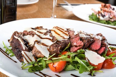 Geleneksel İtalyan ana yemeği. Tagliata bifteği, roka, kiraz domatesleri, Grana Padano talaşı, balzamik redüksiyon. Emilia Romagna bölgesine özgü yiyecekler. Restoran masası kurulumu