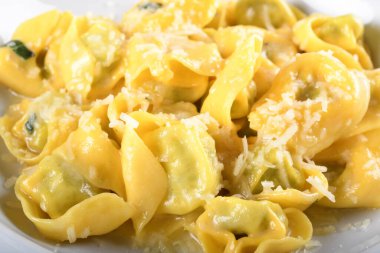 Peynirli ve ıspanaklı Tortellini, tereyağı, adaçayı sosu, rendelenmiş parmesan. Geleneksel İtalyan makarnası üzerine Parmigiano-Reggiano gevrekleri, beyaz tabakta, restoranda kahverengi masada servis ediliyor.