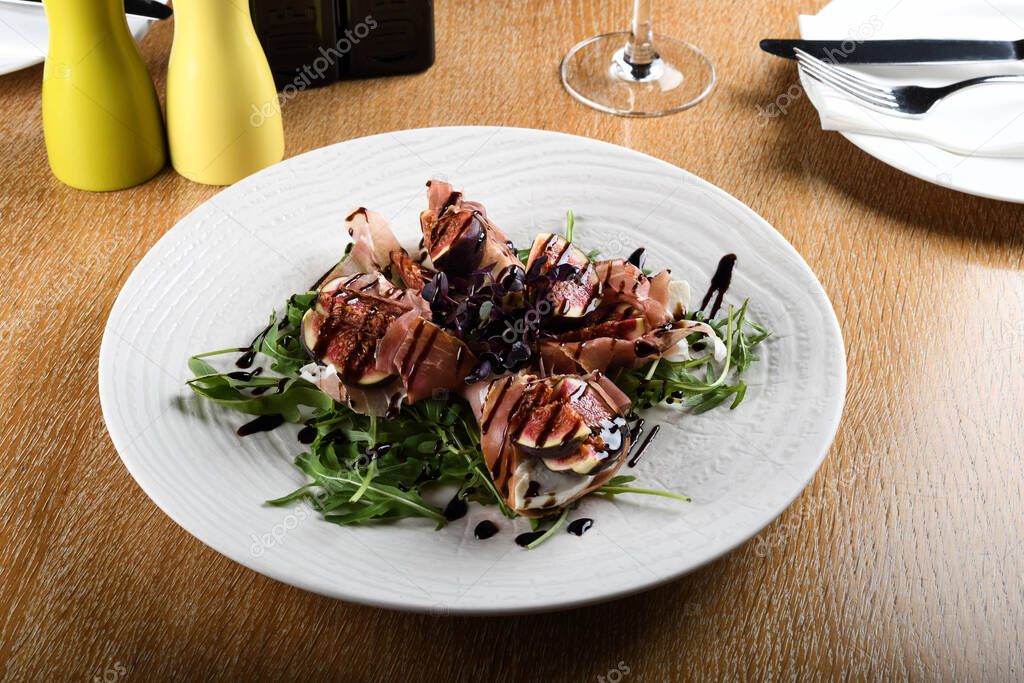 Traditional Italian salad made with figs, Prosciutto dry-cured ham or Parma ham thinly sliced prosciutto crudo served on a white plate in an Italian Restaurant