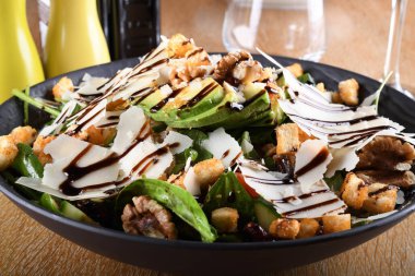 Bebek ıspanak salatası, avokado, kiraz domatesleri, mantarlar, salatalık sosu, kıtır ekmek, parmezan, kavrulmuş ceviz, kahverengi ahşap bir masada servis edilen siyah bir kase, İtalyan restoranı.