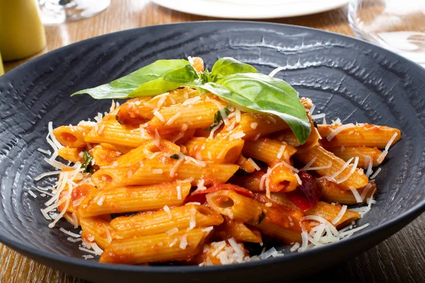 Napoli usulü makarna, geleneksel İtalyan mutfağı, kırmızı biber, domates ve parmesan sosu, beyaz ya da siyah tabakta, restoran ortamında. Penne al 'arrabiata (baharatlı domates soslu makarna)