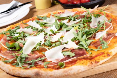 Taze fırın geleneksel prosciutto, roka, domates ve parmesan pizza, ahşap bir tahtanın üzerinde servis edilir.