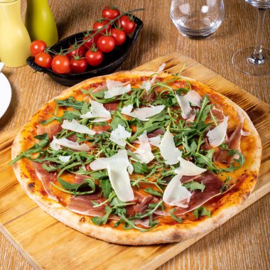 Taze fırın geleneksel prosciutto, roka, domates ve parmesan pizza, ahşap bir tahtanın üzerinde servis edilir.