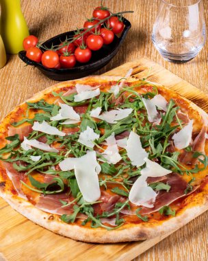 Taze fırın geleneksel prosciutto, roka, domates ve parmesan pizza, ahşap bir tahtanın üzerinde servis edilir.