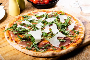 Taze fırın geleneksel prosciutto, roka, domates ve parmesan pizza, ahşap bir tahtanın üzerinde servis edilir.
