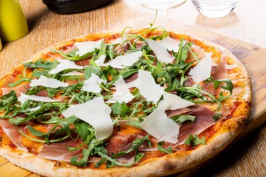 Taze fırın geleneksel prosciutto, roka, domates ve parmesan pizza, ahşap bir tahtanın üzerinde servis edilir.