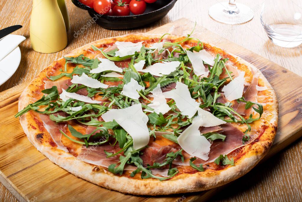 Fresh oven baked traditional prosciutto, rucola, tomato and parmesan pizza, served on a wooden board