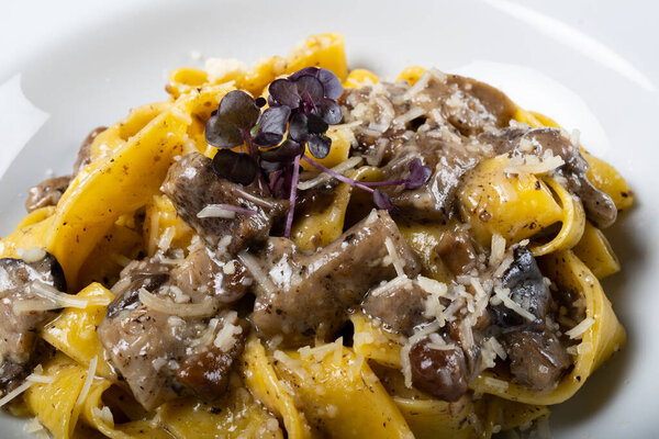 Fresh pappardelle pasta with porcini mushrooms and truffle scent. Traditional italian dish cooked in italian style and spices. Parmesan and mozzarella cheese sauce dressing. Restaurant table setting.
