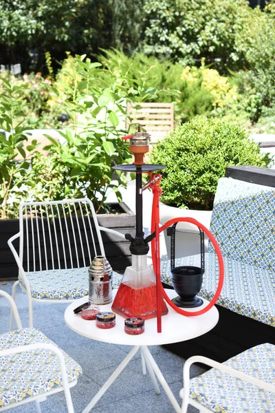 Shisha hookah on restaurant table in the garden. Metal hookah on a summer terrace with a blurred background.