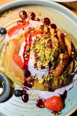 Restoran ortamında servis edilen kibrit tozu krepleri, üzerinde dondurma, çilek ve çikolata sosları, akçaağaç şurubu ve şam fıstığı ile birlikte.