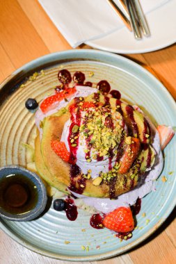 Restoran ortamında servis edilen kibrit tozu krepleri, üzerinde dondurma, çilek ve çikolata sosları, akçaağaç şurubu ve şam fıstığı ile birlikte.