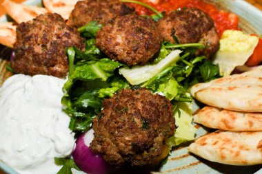 Salatalı Akdeniz köftesi, domates soslu nohut, yoğurt sosu ve arka plandaki ahşap masada servis edilen Pita ekmeği..
