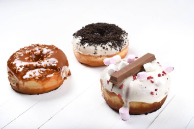 Üç erimiş çikolata, lokum, bisküvi parçacıkları, beyaz tahta üzerinde karamel şekerli çörekler.