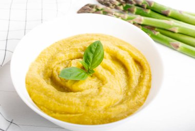 Beyaz ahşap zemin üzerinde taze yeşil kuşkonmaz kremalı çorba.