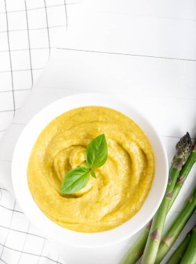 Beyaz ahşap zemin üzerinde taze yeşil kuşkonmaz kremalı çorba.