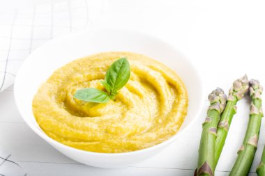 Beyaz ahşap zemin üzerinde taze yeşil kuşkonmaz kremalı çorba.