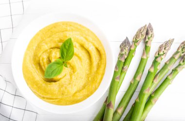 Beyaz ahşap zemin üzerinde taze yeşil kuşkonmaz kremalı çorba.