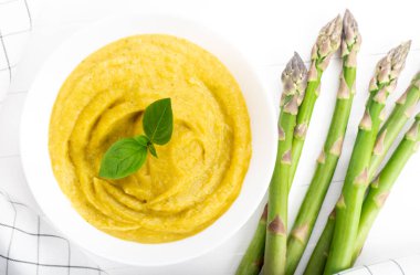 Beyaz ahşap zemin üzerinde taze yeşil kuşkonmaz kremalı çorba.