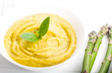 Beyaz ahşap zemin üzerinde taze yeşil kuşkonmaz kremalı çorba.