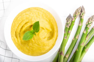 Beyaz ahşap zemin üzerinde taze yeşil kuşkonmaz kremalı çorba.