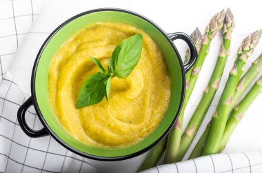 Beyaz ahşap zemin üzerinde taze yeşil kuşkonmaz kremalı çorba.