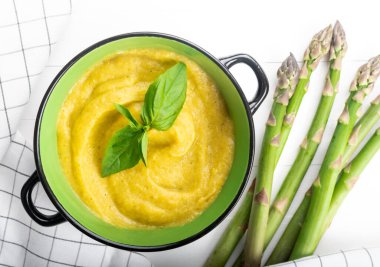 Beyaz ahşap zemin üzerinde taze yeşil kuşkonmaz kremalı çorba.