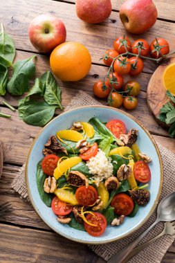 Ispanaklı, portakallı, kiraz domatesli, cevizli, incirli, kinoalı, arkaplanda taze meyve mandalinalı, ahşap tahtada, kırsal peçetede ve yakın ve üst görüşlü tatlı salata.