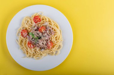 Spagetti, sarı arka planda malzemelerle birlikte makarna pişirdi. Renkli bluz ve geleneksel İtalyan yemeği kasesinin yakın görüntüsü. Terfi için fotokopi alanı olan düz dizayn kavramı