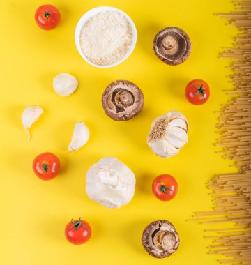 Sarı arka planda makarna pişirmek için malzemeli spagetti makarna. Renkli üst ve İtalyan yemeği için ham malzemelerin yakın çekim görüntüsü. Terfi için fotokopi alanı olan düz dizayn kavramı
