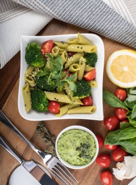 Tahtada izole edilmiş yeşil bezelyelerden yapılmış glütensiz pişmiş makarna. Fesleğen, domates, avokado ve kişniş. Yukarıdan ateş edilmiş ve yakın plan. yemek arkaplanı İtalyan makarna