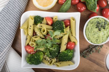 Tahtada izole edilmiş yeşil bezelyelerden yapılmış glütensiz pişmiş makarna. Fesleğen, domates, avokado ve kişniş. Yukarıdan ateş edilmiş ve yakın plan. yemek arkaplanı İtalyan makarna