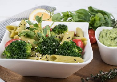 Tahtada izole edilmiş yeşil bezelyelerden yapılmış glütensiz pişmiş makarna. Fesleğen, domates, avokado ve kişniş. Yukarıdan ateş edilmiş ve yakın plan. yemek arkaplanı İtalyan makarna