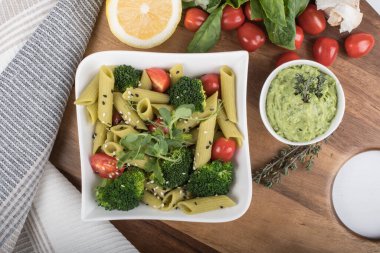 Tahtada izole edilmiş yeşil bezelyelerden yapılmış glütensiz pişmiş makarna. Fesleğen, domates, avokado ve kişniş. Yukarıdan ateş edilmiş ve yakın plan. yemek arkaplanı İtalyan makarna