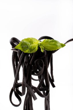 Çatalla izole edilmiş siyah taze tagliatelle makarna (mürekkep balığı mürekkebiyle yapılmış makarna) fesleğen yaprağı, basit beyaz tabak ve temiz beyaz arka plan üzerinde