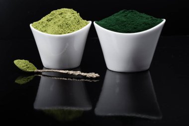 Beyaz ve kırsal arka planda kurumuş organik buğday ve spirulina tozu içeren izole bir çorba kaşığı. Sağlıklı yaşam, detoks tarifleri, çiğ vejetaryen içeceği veya meyve suyu malzemeleri.