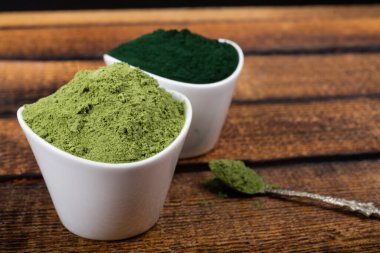 Beyaz ve kırsal arka planda kurumuş organik buğday ve spirulina tozu içeren izole bir çorba kaşığı. Sağlıklı yaşam, detoks tarifleri, çiğ vejetaryen içeceği veya meyve suyu malzemeleri.