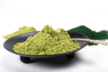 Beyaz ve kırsal arka planda kurumuş organik buğday ve spirulina tozu içeren izole bir çorba kaşığı. Sağlıklı yaşam, detoks tarifleri, çiğ vejetaryen içeceği veya meyve suyu malzemeleri.