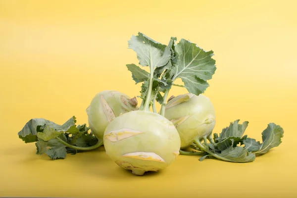 Three pieces of kohlrabi vegetable isolated on yellow simple background with copy space. Green leafy vegetable from cabbage and radish family, bio and organic grown from the garden