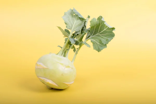 Three pieces of kohlrabi vegetable isolated on yellow simple background with copy space. Green leafy vegetable from cabbage and radish family, bio and organic grown from the garden