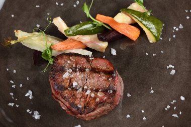 Pirzola bifteği, mevsimlik sebzeler ve arka planda patates kızartması. Restoran masasında servis edilen lüks yemek tabağı. Taze etli biftek.