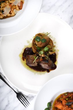 Kuzu pirzolası, fırında patates, enginar sote ve kırmızı şarap sosu. Geleneksel İtalyan yemeği. Restoran masasında servis edilen orijinal yemek. Arka plandaki diğer yemekler bulanık