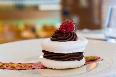 Üzerinde koyu çikolata ve çilek olan kremalı pasta, aristaurant bir ortamda, bulanık arka planda.